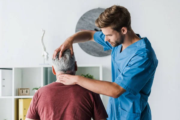 Guapo médico tocando cabeza de paciente de mediana edad en clínica - foto de stock