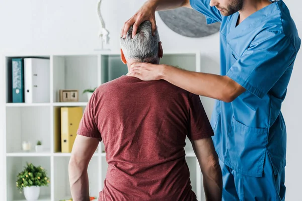 Ausgeschnittene Ansicht eines bärtigen Arztes, der Kopf einer Patientin mittleren Alters in Klinik berührt — Stockfoto