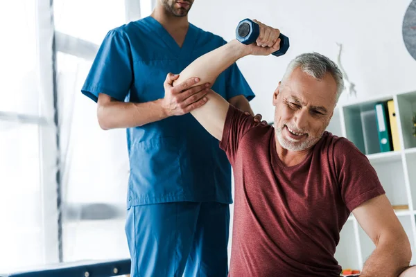 Cropped view of doctor near mature man working out with dumbbell — Stock Photo