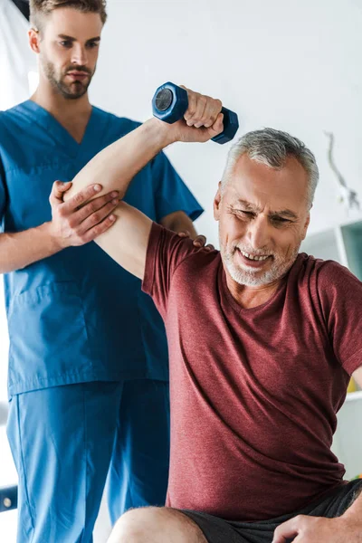 Focalizzazione selettiva di felice uomo maturo che lavora con manubri vicino al medico — Foto stock