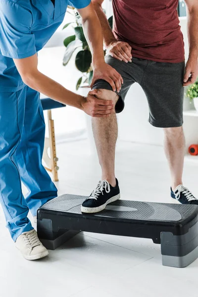 Ausgeschnittene Ansicht des Arztes, der Knie eines reifen Patienten auf Trittplattform berührt — Stockfoto
