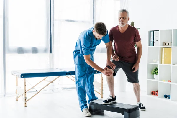 Schöner Arzt berührt Knie der reifen Patienten auf Schritt Plattform — Stockfoto