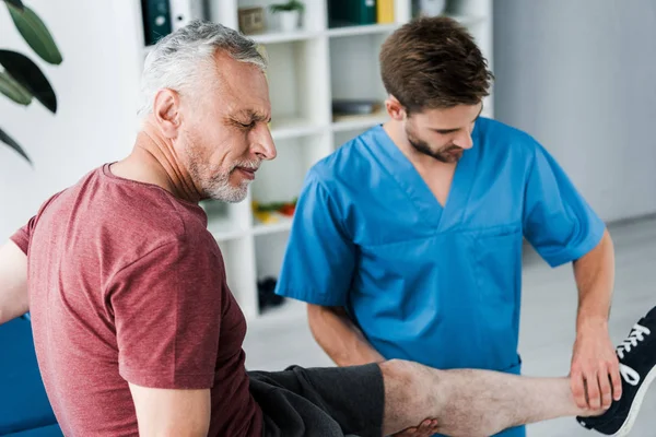 Selective focus of bearded patient with closed eyes and pain near doctor — Stock Photo