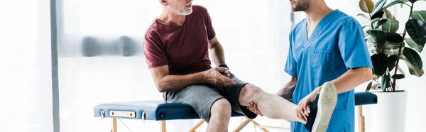 Panoramaaufnahme von Arzt, der Bein einer reifen Patientin berührt — Stockfoto