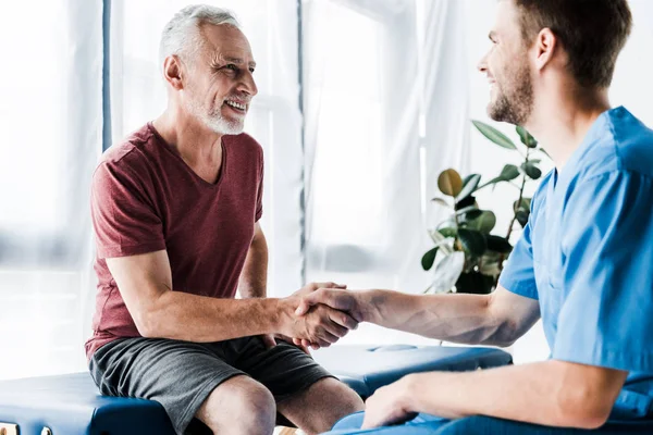 Enfoque selectivo del paciente feliz estrechando la mano con el médico - foto de stock