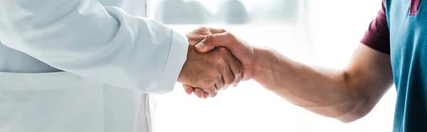 Panoramic shot of doctor in white coat shaking hands with man — Stock Photo