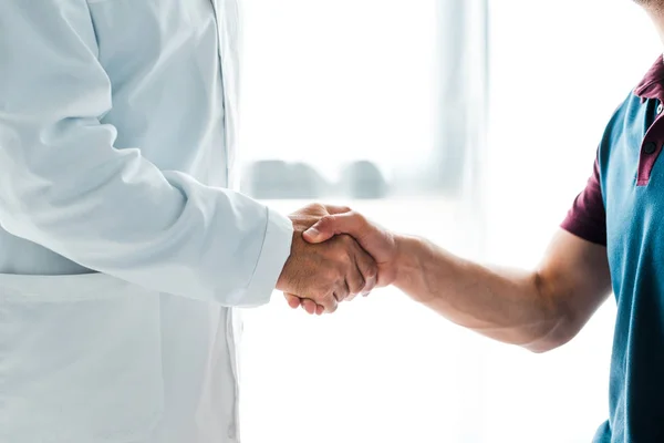 Cropped view of doctor in white coat shaking hands with man — Stock Photo