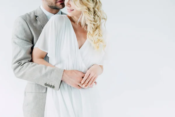 Vista recortada de la novia y el novio abrazando y sosteniendo las manos aisladas en gris - foto de stock
