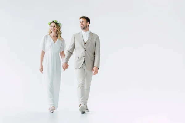 Привлекательная невеста и красивый жених держась за руки и глядя в сторону — стоковое фото