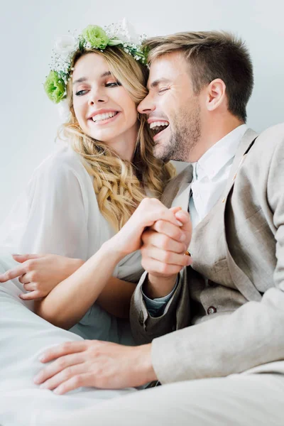 Atractiva novia y novio guapo tomados de la mano y mirando hacia otro lado aislado en gris - foto de stock