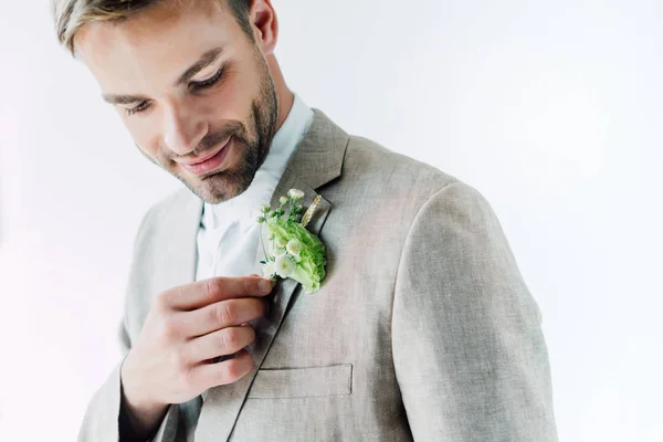 Beau marié en costume tenant boutonnière florale et la regardant isolé sur gris — Photo de stock