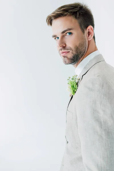 Bello sposo in abito con boutonniere floreale guardando la fotocamera isolata su grigio — Foto stock