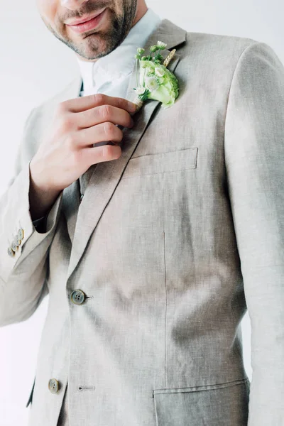 Cropped view of bridegroom in suit holding floral boutonniere isolated on grey — Stock Photo