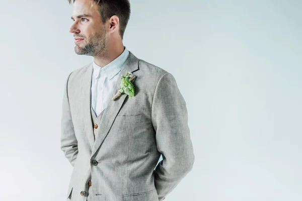 Bello sposo in abito con boutonniere floreale distogliendo lo sguardo isolato sul grigio — Foto stock