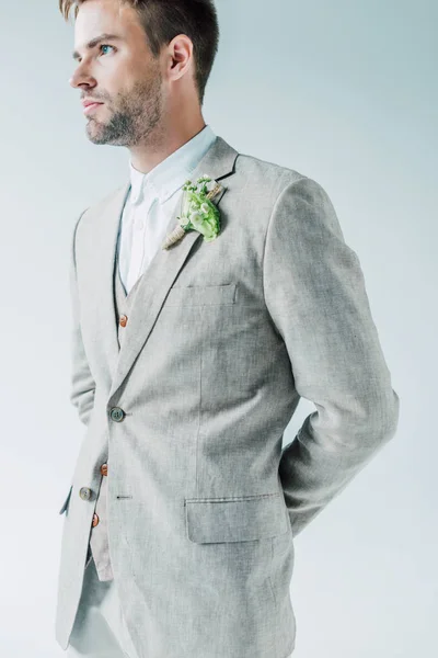 Bello sposo in abito con boutonniere floreale distogliendo lo sguardo isolato sul grigio — Foto stock