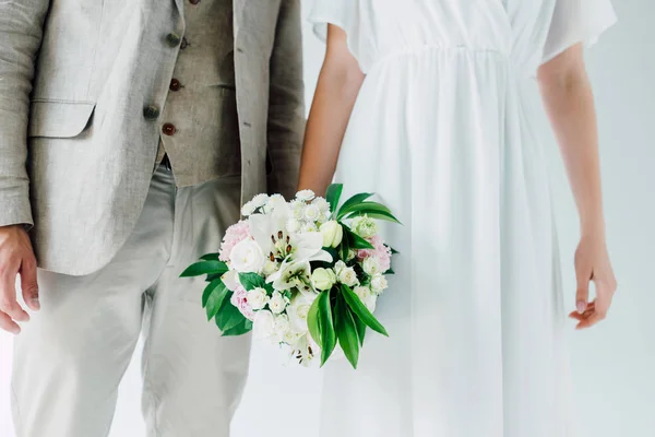 Cropped view of bride with bouquet and bridegroom in suit — Stock Photo