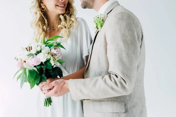 Обрезанный вид невесты и красивого жениха, обнимающего и держащего букет — стоковое фото