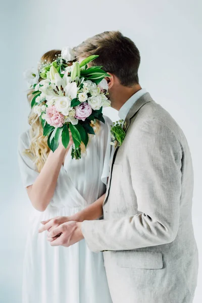Невеста в свадебном платье, обнимающая жениха и держащая букет — стоковое фото