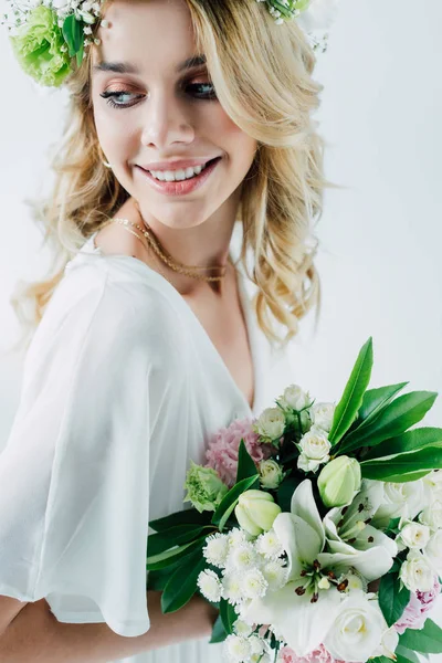 Noiva atraente em vestido de noiva e coroa segurando buquê isolado no branco — Fotografia de Stock