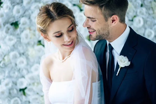 Novia atractiva y novio guapo sonriendo y mirándose el uno al otro - foto de stock