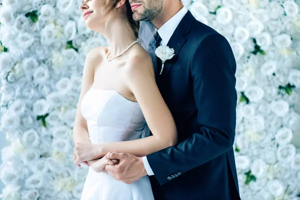 Обрезанный вид невесты в свадебном платье обнимающей с женихом — стоковое фото
