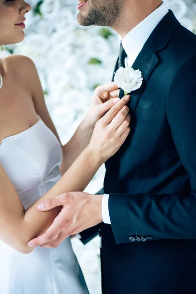 Cropped view of bride in wedding dress holding buttonhole of her bridegroom — Stock Photo
