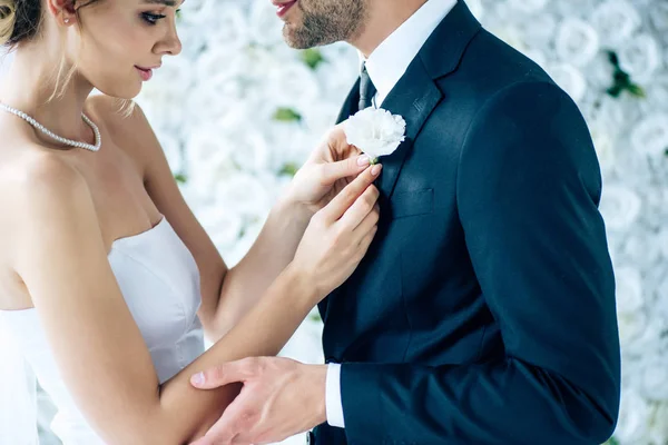 Vista cortada da noiva em vestido de noiva segurando botão de seu noivo — Fotografia de Stock