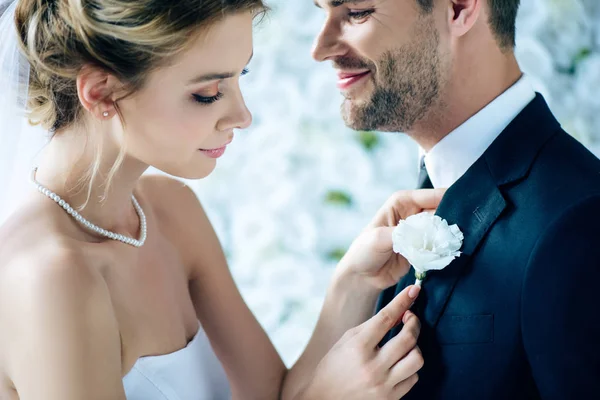 Attractive bride in wedding dress holding buttonhole of her bridegroom — Stock Photo