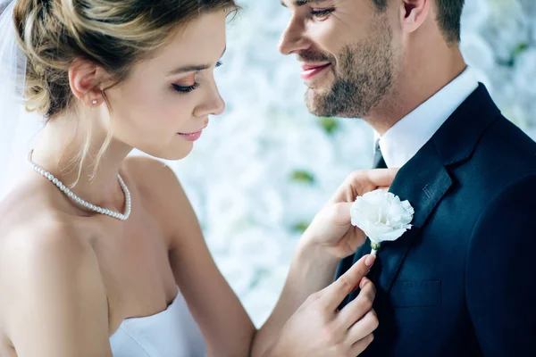 Belle mariée en robe de mariée tenant boutonnière de son marié — Photo de stock