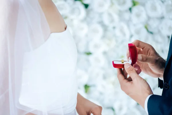 Vista ritagliata dello sposo che mostra scatola regalo rossa alla sposa — Foto stock