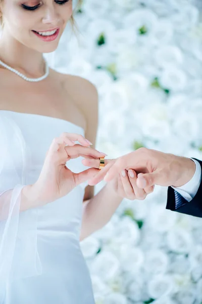 Привлекательная и улыбающаяся невеста надевает обручальное кольцо на палец — стоковое фото