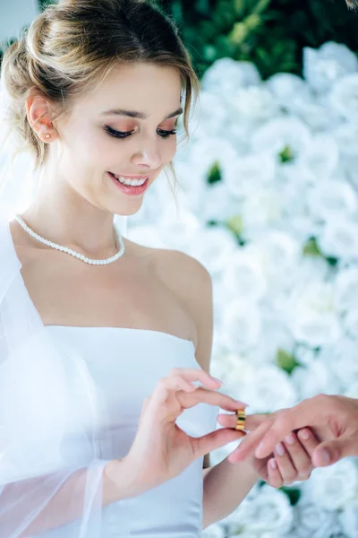 Atractiva y sonriente novia poniendo anillo de bodas en el dedo - foto de stock