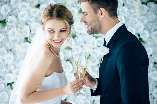 Attractive bride and handsome bridegroom smiling and clinking with champagne glasses — Stock Photo