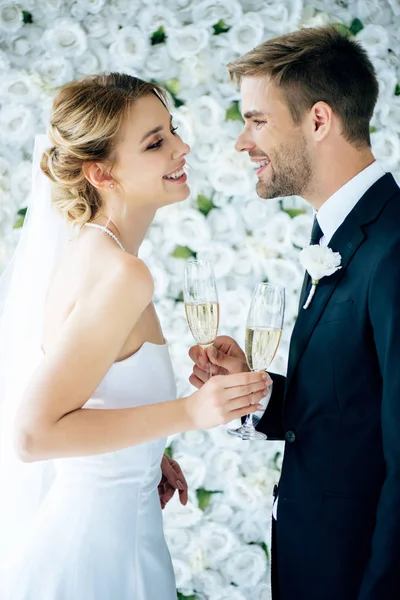 Novia atractiva y novio guapo sonriendo y tintineo con copas de champán - foto de stock