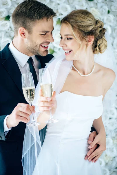 Attraktive Braut und schöner Bräutigam lächeln und klirren mit Champagnergläsern — Stockfoto