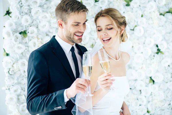 Привлекательная невеста и красивый жених, улыбающийся и звенящий с бокалами шампанского — стоковое фото