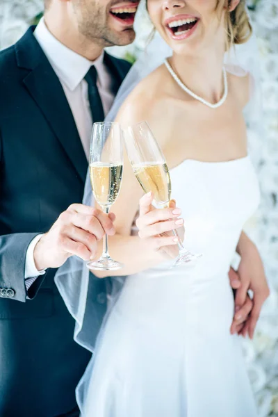 Cropped view of bride and bridegroom clinking with champagne glasses — Stock Photo