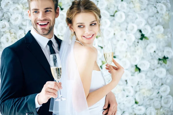 Novia atractiva y novio guapo sonriendo y sosteniendo copas de champán - foto de stock