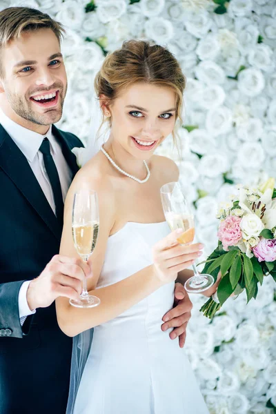 Novia atractiva y novio guapo sonriendo y sosteniendo copas de champán - foto de stock
