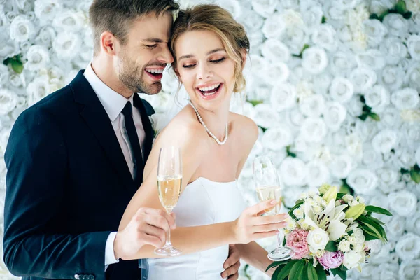 Привлекательная невеста и красивый жених улыбаясь и держа бокалы шампанского — стоковое фото