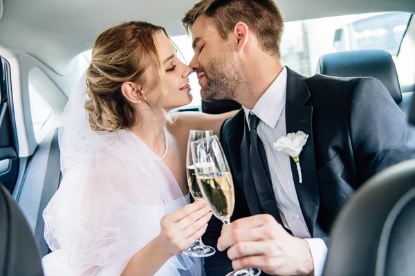 Atractiva novia y guapo novio besos y tintineo con copas de champán - foto de stock