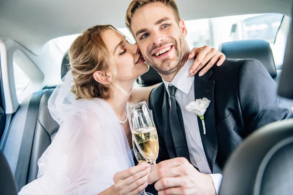 Attractive bride and handsome bridegroom kissing and clinking with champagne glasses — Stock Photo