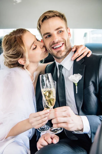 Atractiva novia y guapo novio besos y tintineo con copas de champán - foto de stock
