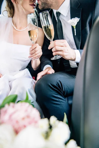 Cropped view of bride and bridegroom kissing and clinking with champagne glasses — Stock Photo