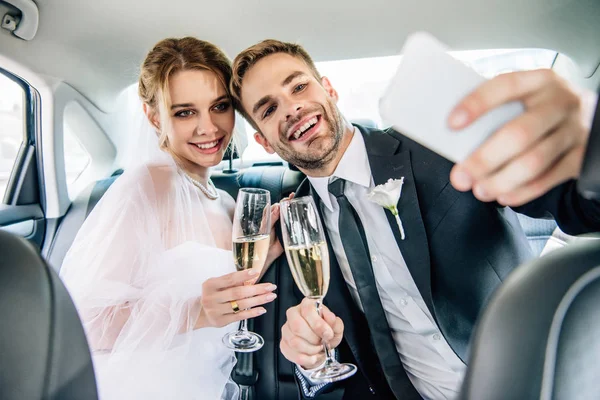 Mariée attrayante et beau marié prenant selfie en voiture — Photo de stock