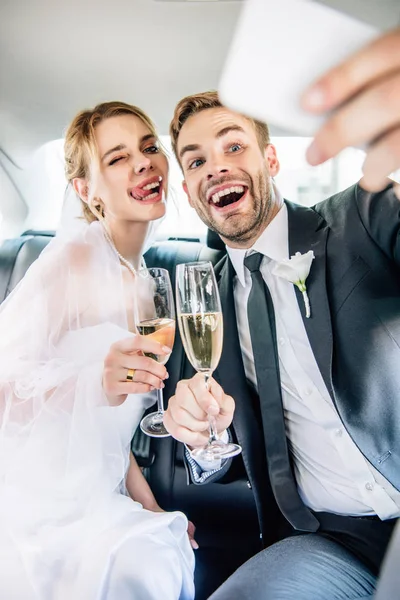 Attraktive Braut und schöner Bräutigam machen Selfie im Auto — Stockfoto