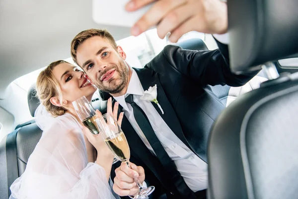 Attractive bride and handsome bridegroom taking selfie in car — Stock Photo