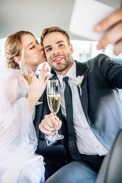 Attractive bride and handsome bridegroom taking selfie in car — Stock Photo