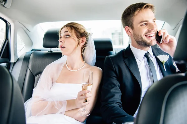 Attractive bride looking away and handsome bridegroom talking on smartphone — Stock Photo