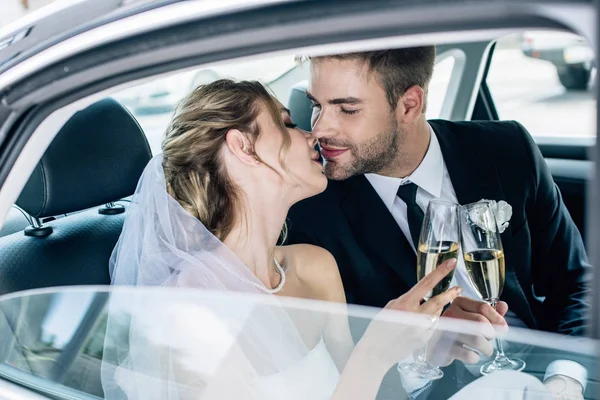 Atractiva novia y guapo novio besos y tintineo con copas de champán - foto de stock